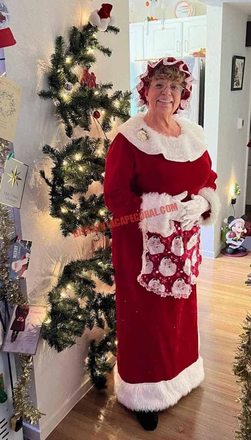 Mrs. Claus for hire in Cape Coral, FL standing beside a lit Christmas tree in a hallway.