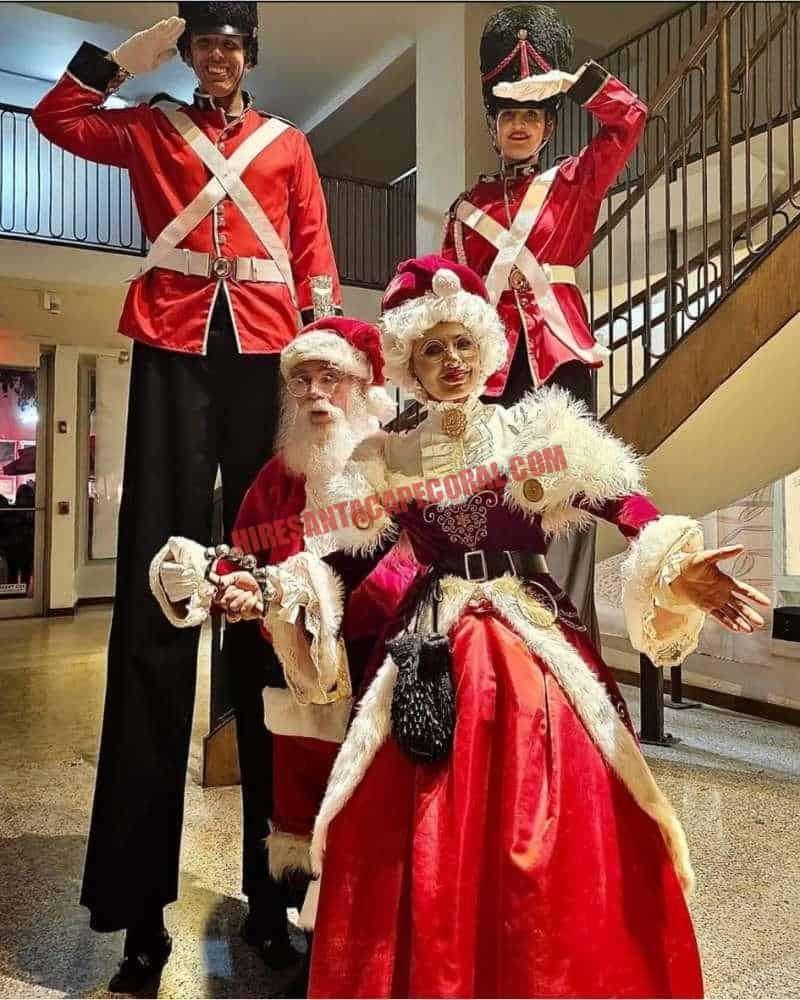 Corporate Santa in Cape Coral, FL with Mrs. Claus and two stilt nutcracker soldiers by a staircase.