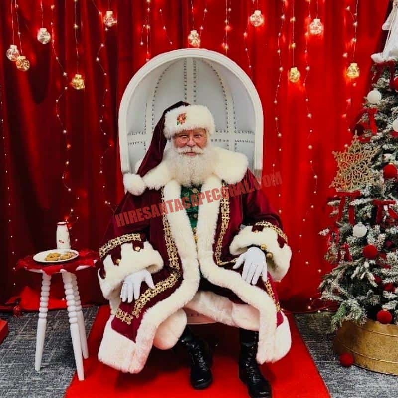 Santa for hire in Fort Myers, FL seated in a white chair with cookies and milk beside a tree.