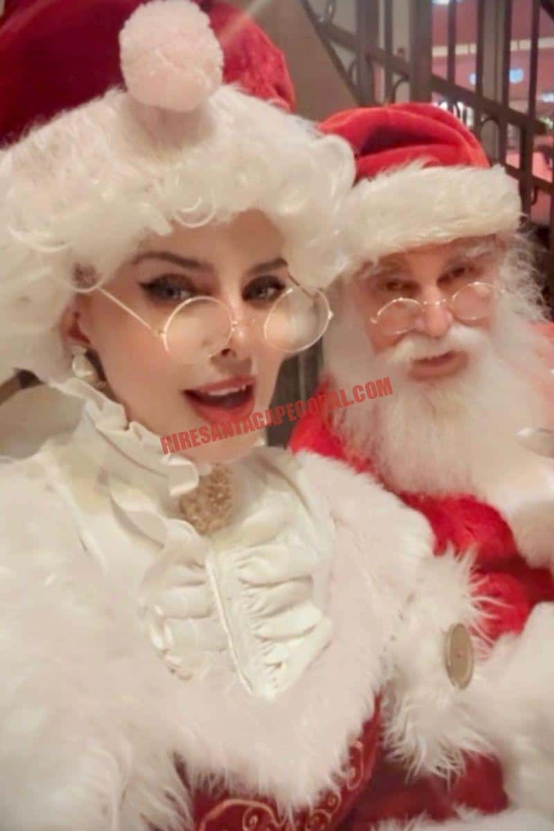 About Hire Santa Cape Coral: Mrs. Claus standing close to Santa in a red suit indoors.